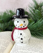 Snowman figurine with a black top hat and red scarf on an open book with greenery in the background